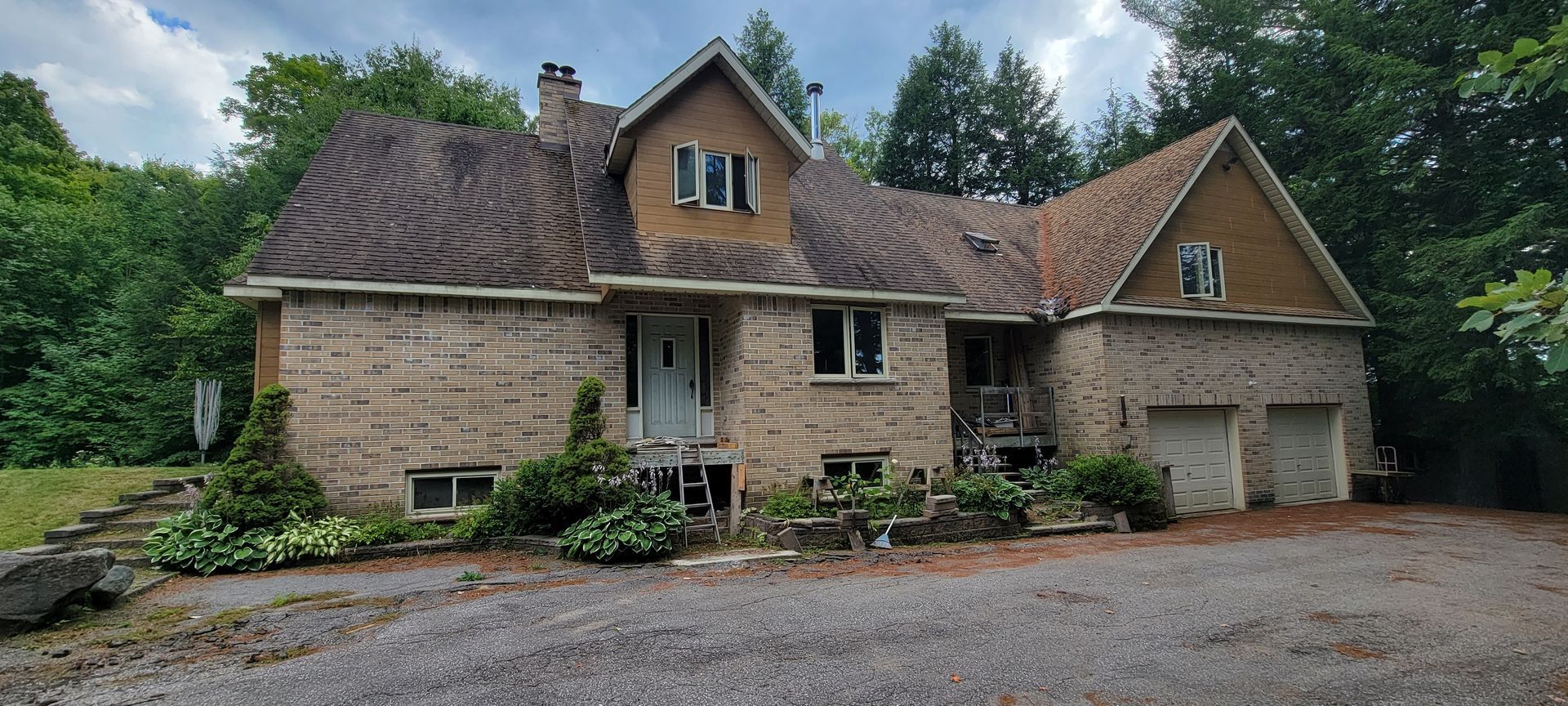 A large brick house with a brown roof is surrounded by trees.