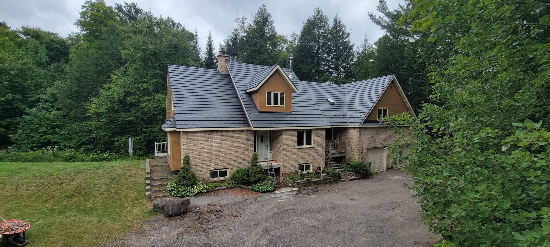 A large brick house is surrounded by trees and a gravel driveway.