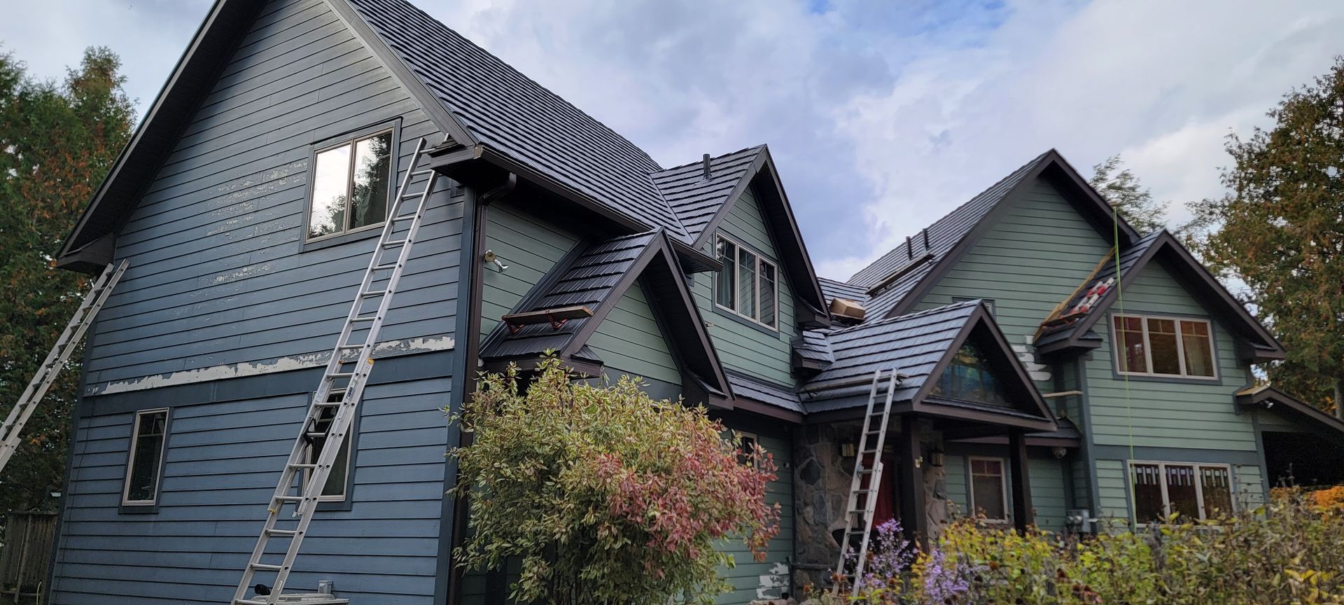 A large house with a ladder on the side of it is being painted.