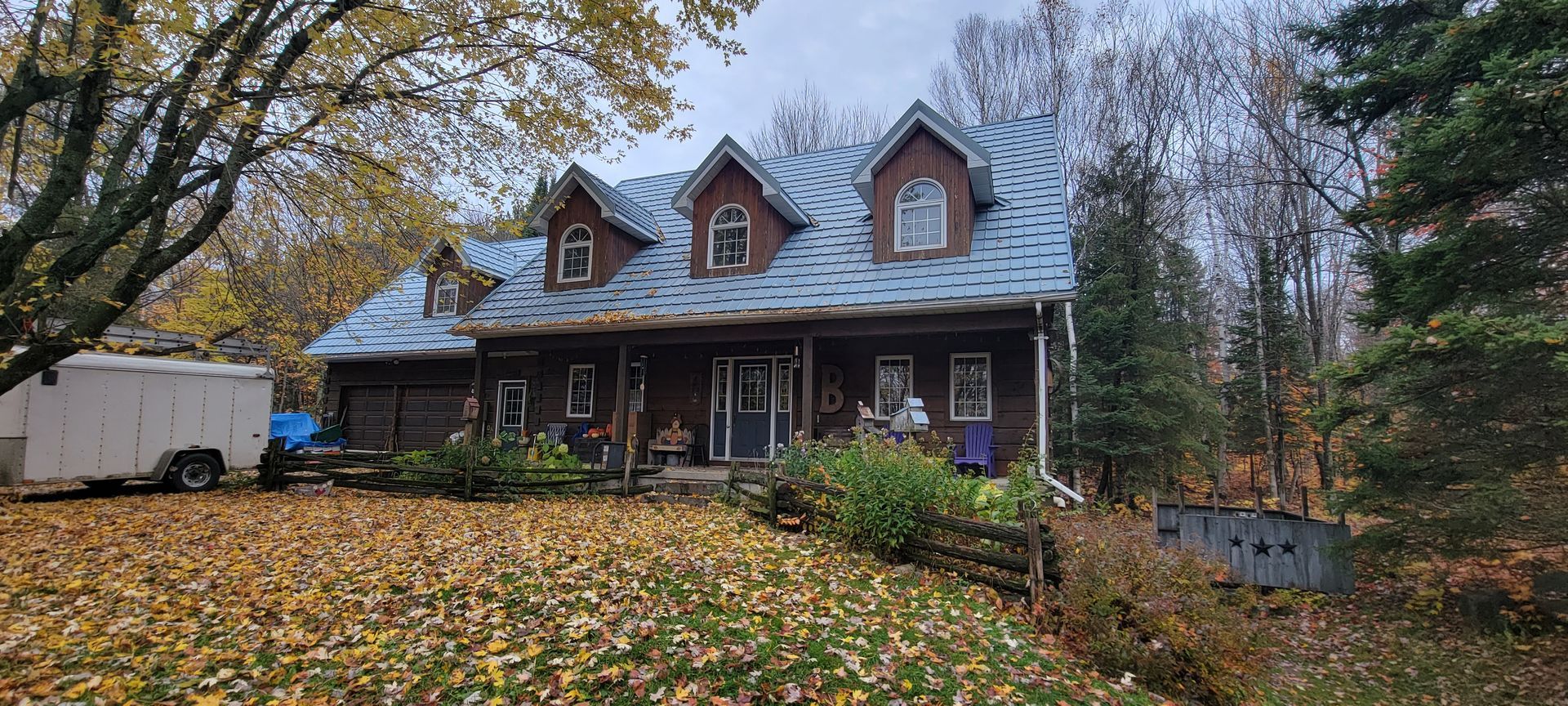 A large house with a blue roof is surrounded by trees and leaves.