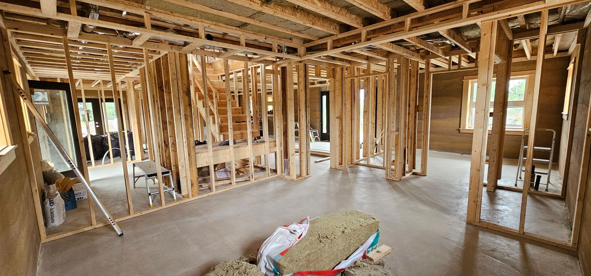 A large room in a house under construction with a bag of insulation on the floor.