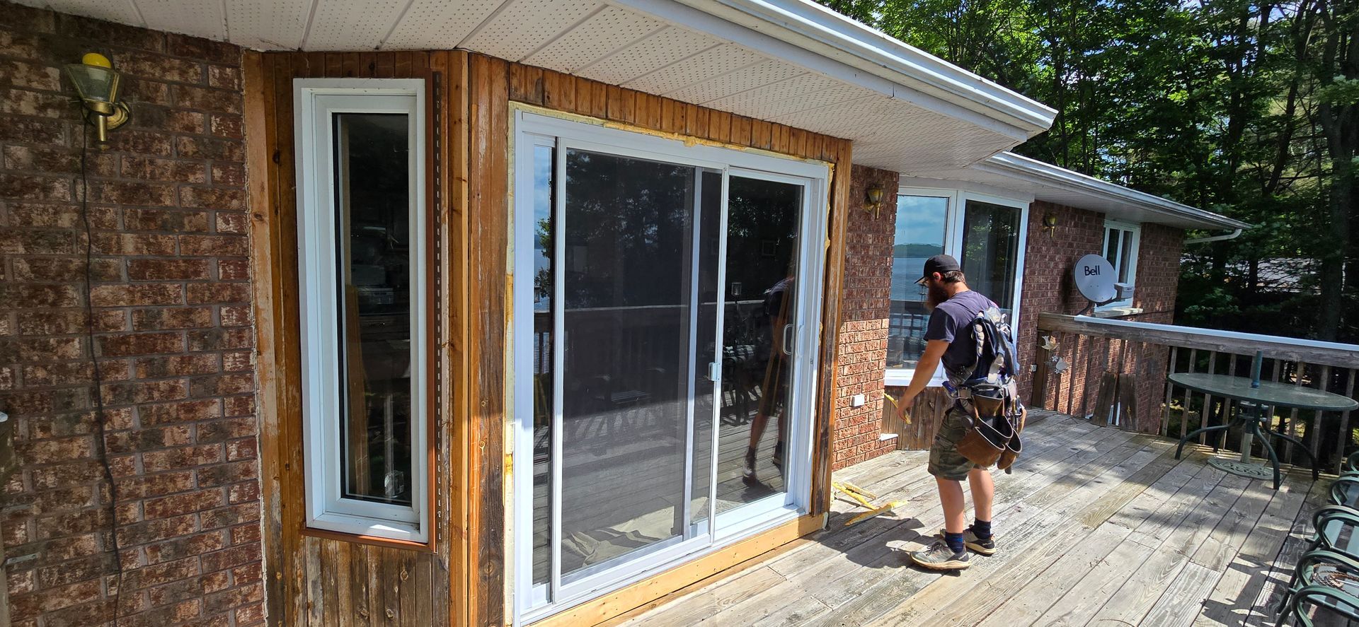 A person on a wooden deck cleans the window of a house with brown siding.