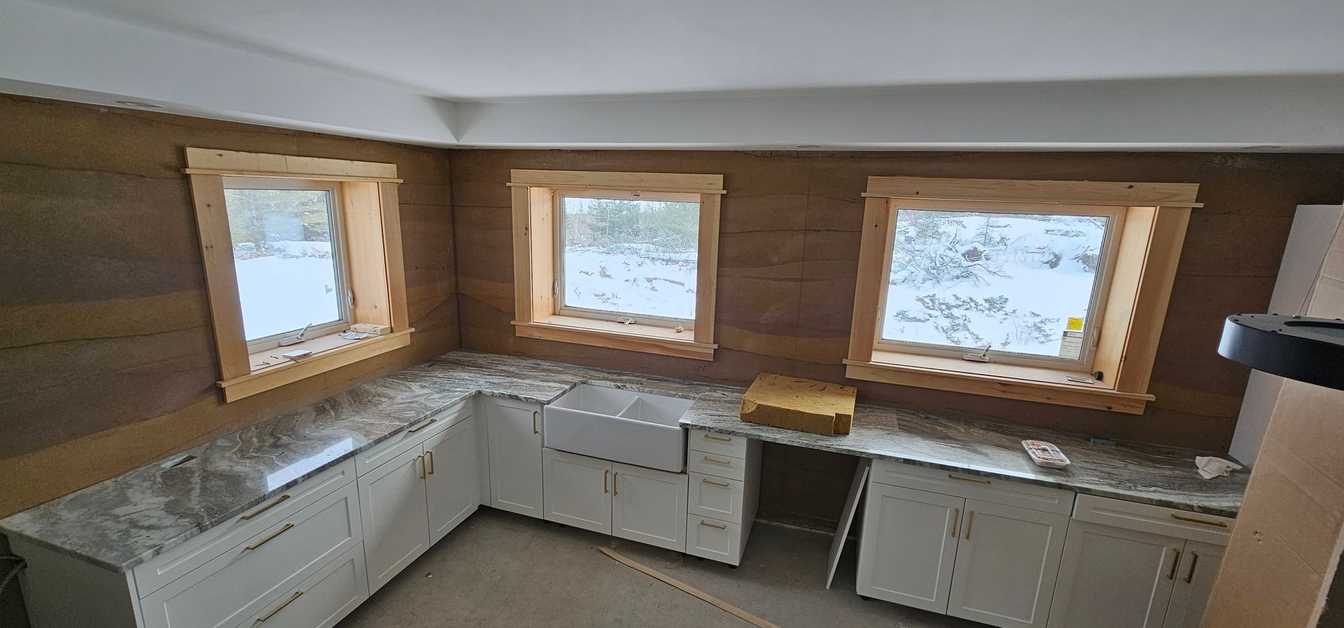 A kitchen with white cabinets , granite counter tops , and three windows.