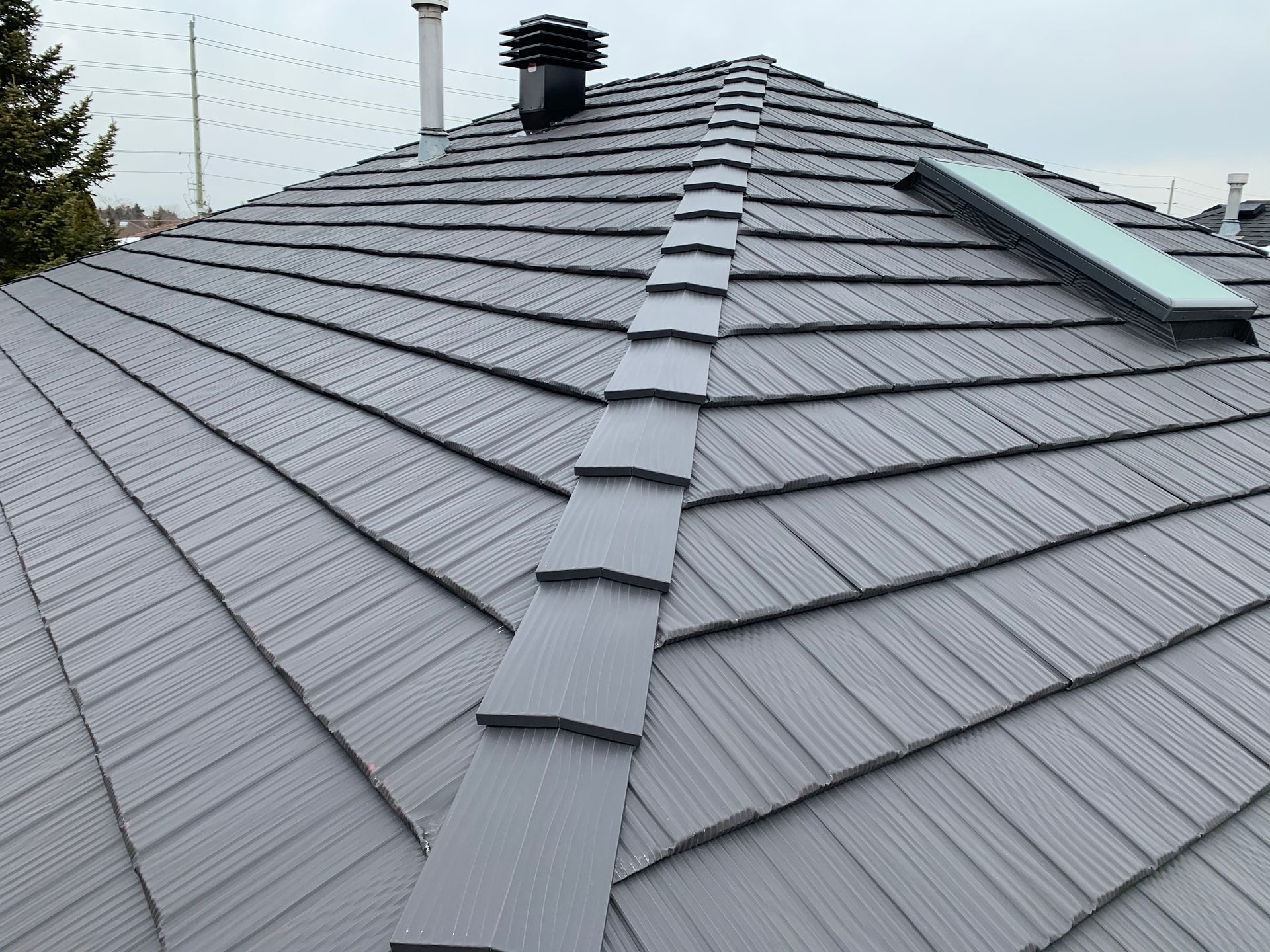 Gray tiled roof with a central ridge cap and rooftop vents under an overcast sky