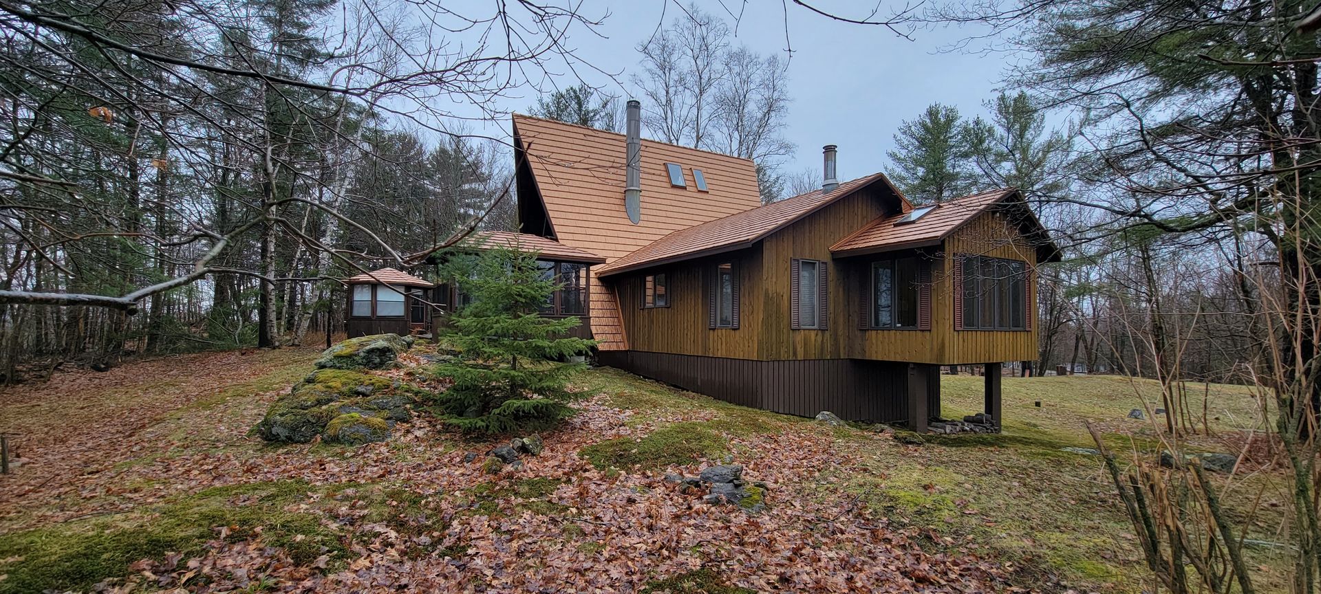 Rustic wooden cabin with a steep roof in a leaf-covered forest clearing