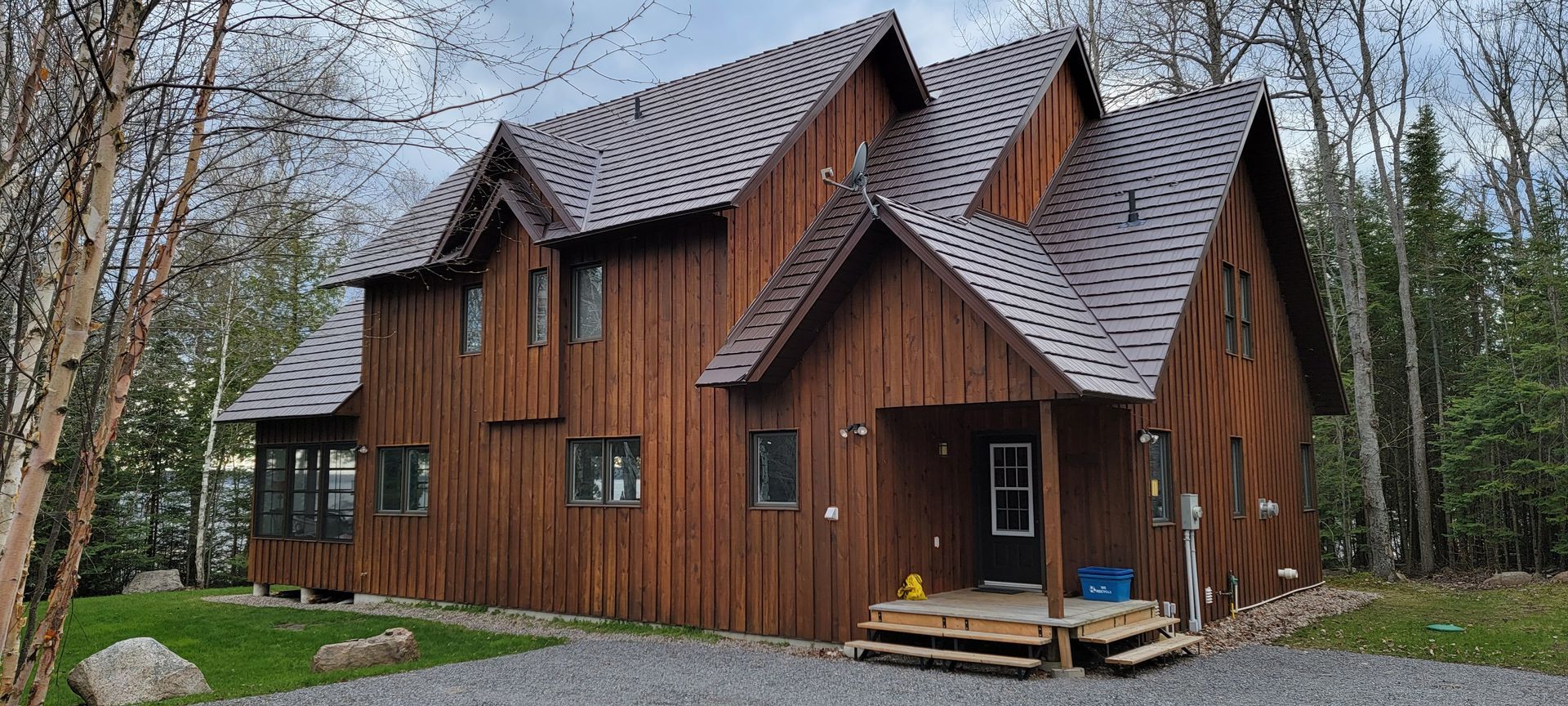 A large wooden house with a gray roof is in the middle of a forest.