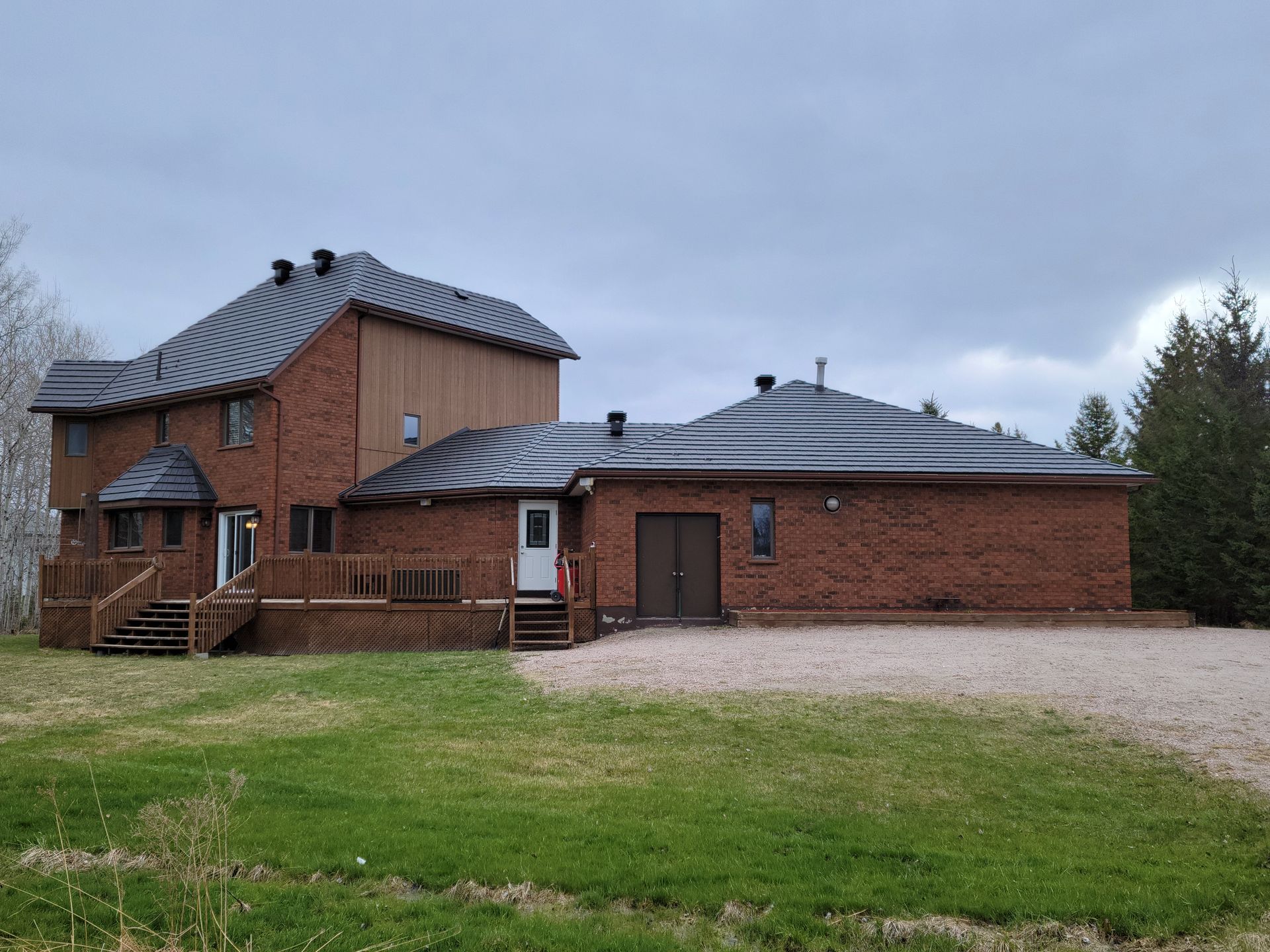 A large brick house with a metal roof is sitting in the middle of a grassy field.