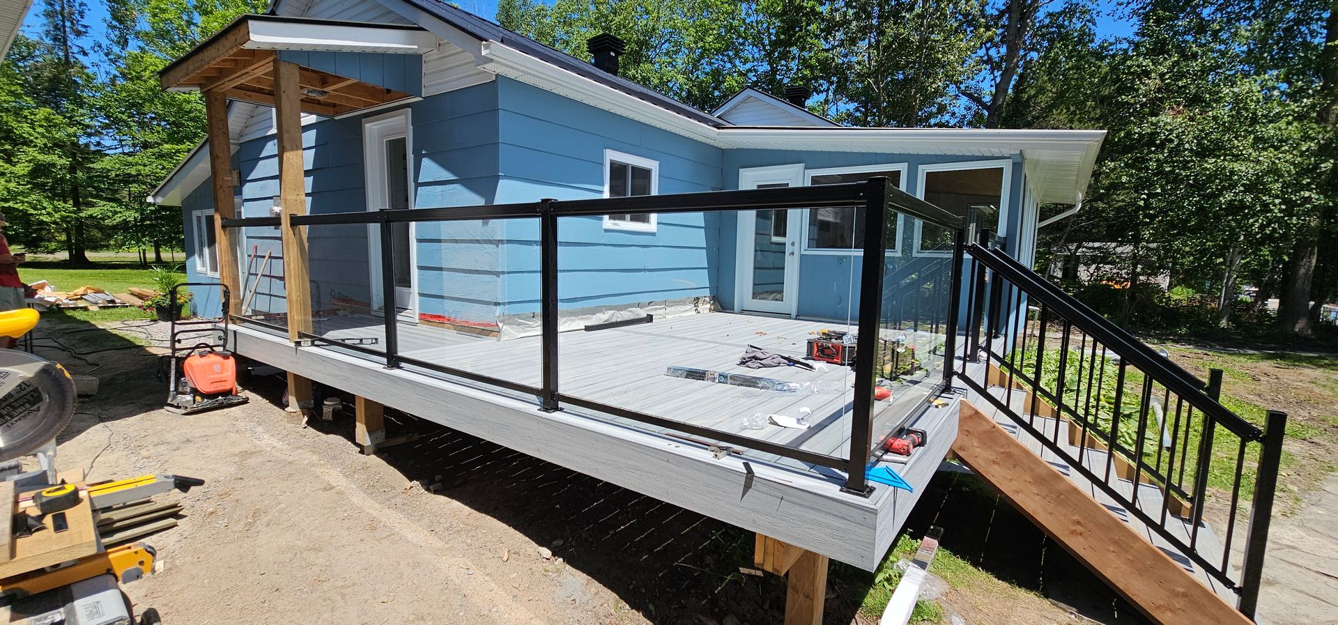 A house with a deck under construction. The deck has black railings, with a ramp and a small pergola.