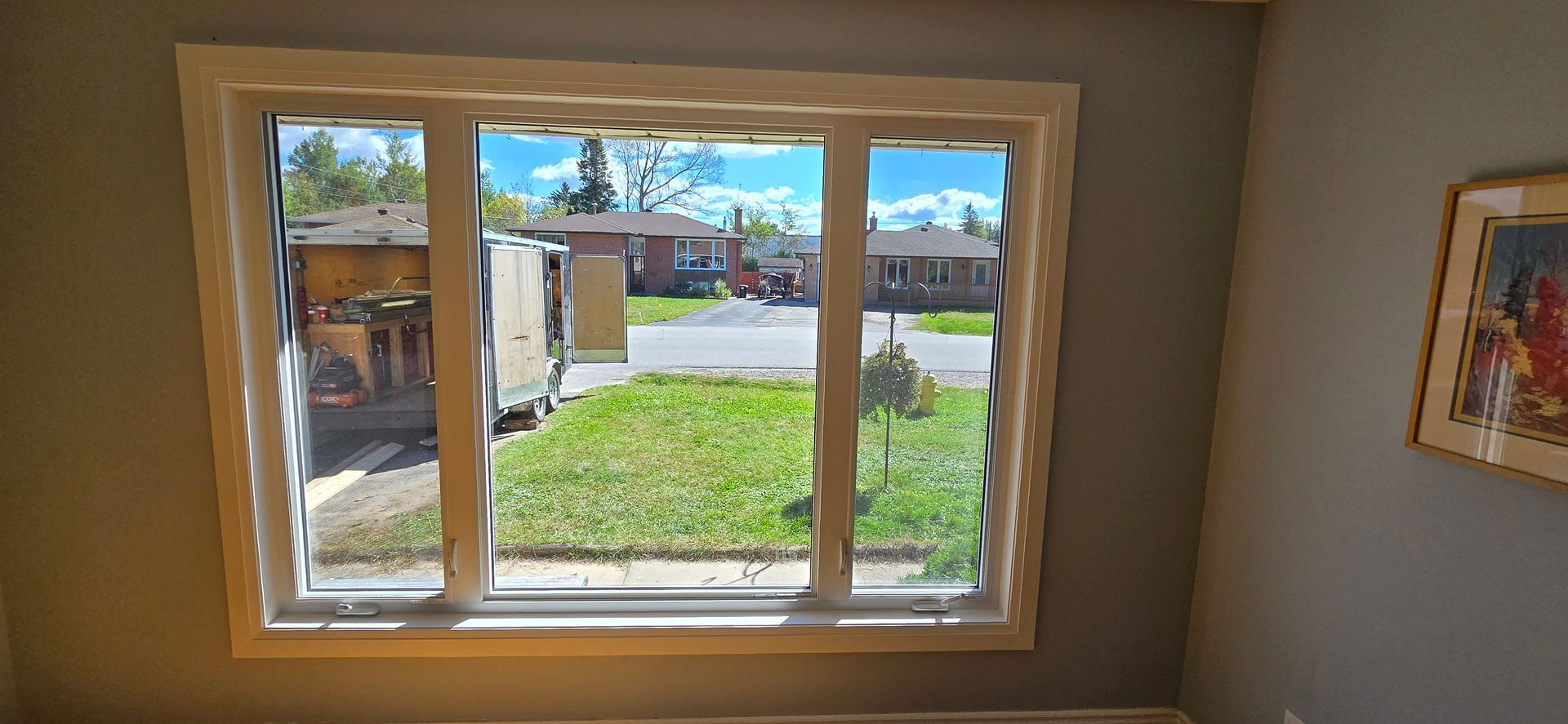 A window frames a view of a street with houses and a grassy lawn, under a blue sky.