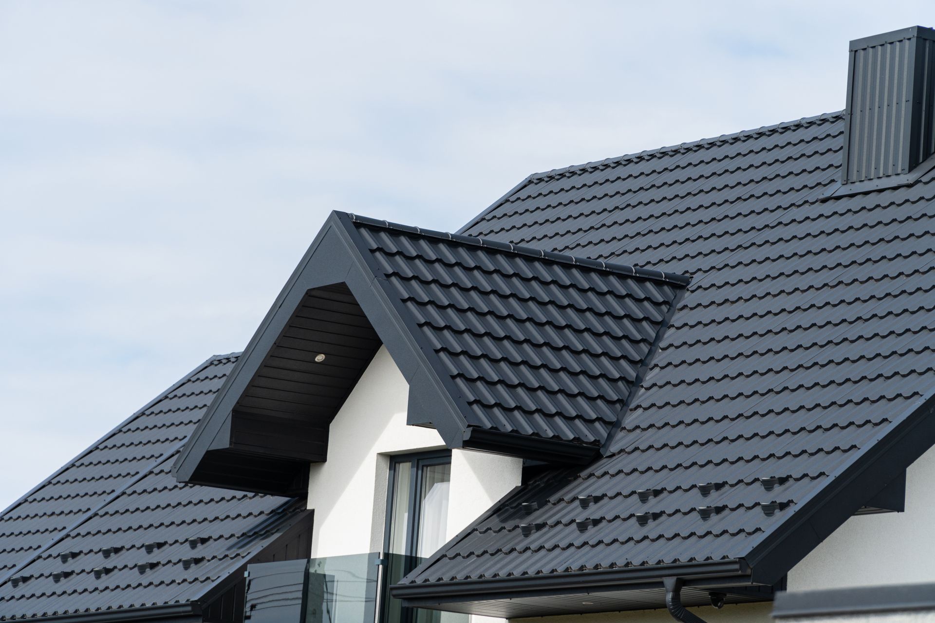 Black metal roof of a white house against a cloudy sky.
