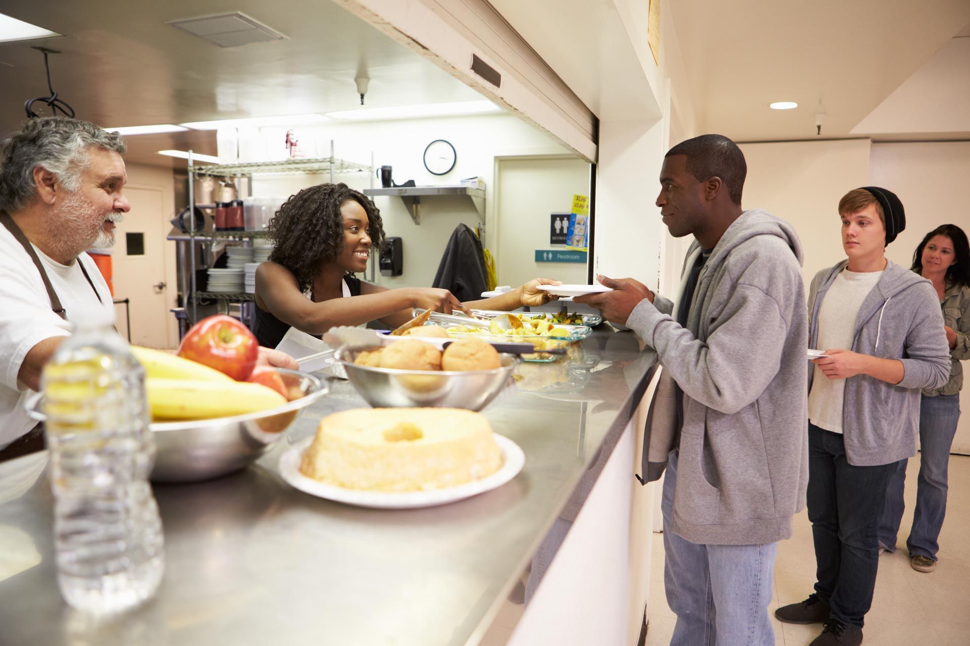a man in a grey sweatshirt is getting food from a woman in a white apron