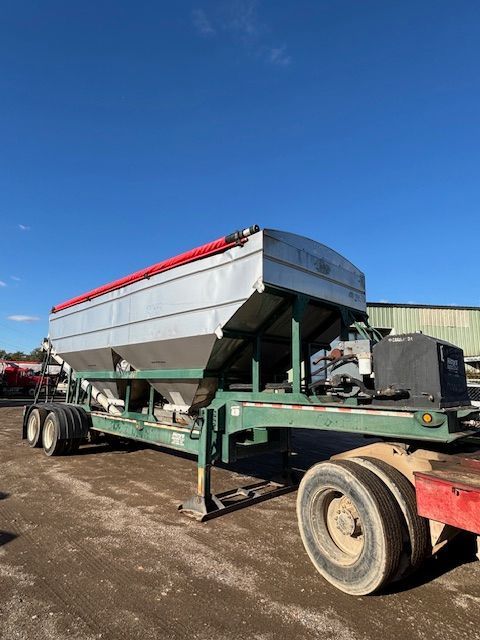 Silver grain trailer with a red tarp, on a gravel lot under a blue sky.