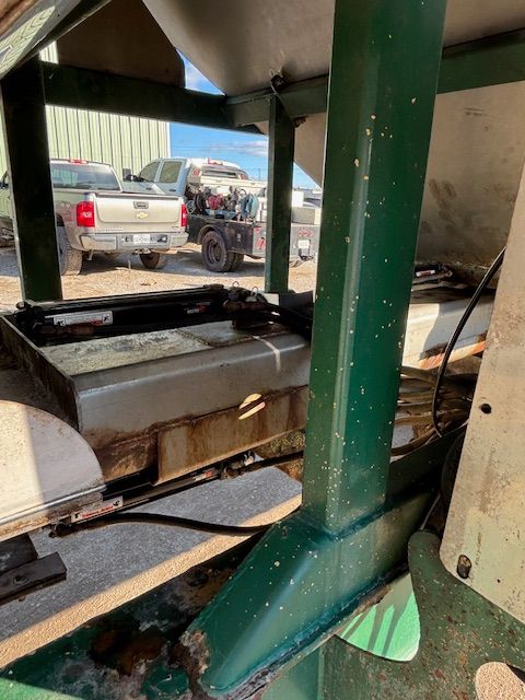 Green and white industrial equipment outdoors, with visible trucks in the background.