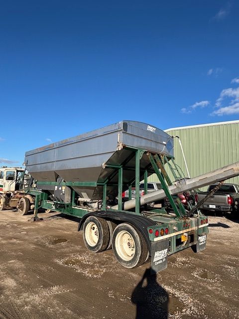 Large silver and green fertilizer spreader trailer under a blue sky.