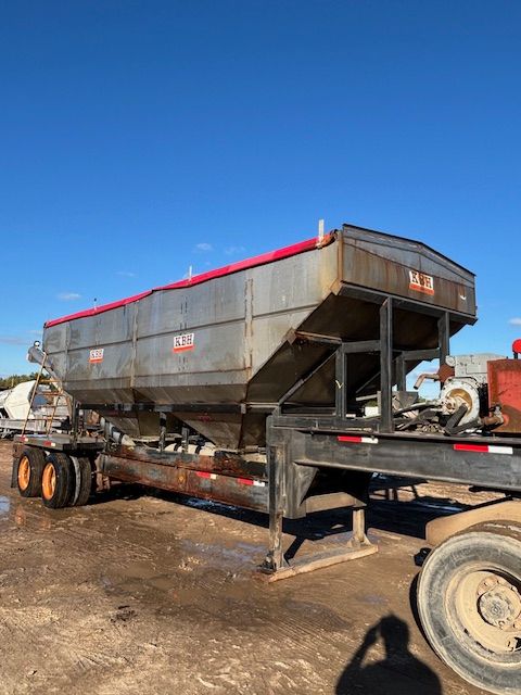 A large silver grain trailer with a red tarp, parked outdoors on a sunny day.