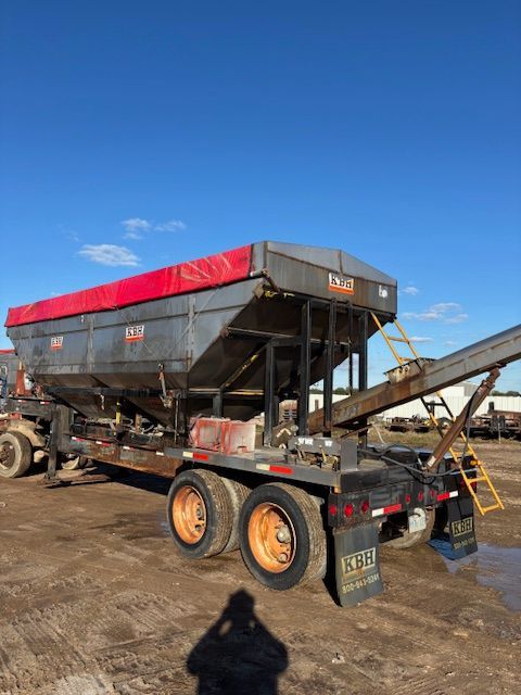 A large, industrial salt spreader trailer with a red tarp cover, sitting on an outdoor lot.
