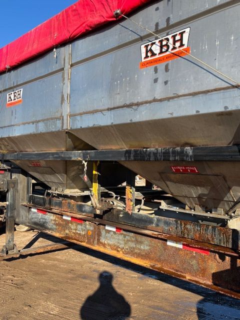 Side view of a KBH branded trailer with a red tarp, likely for hauling bulk materials.