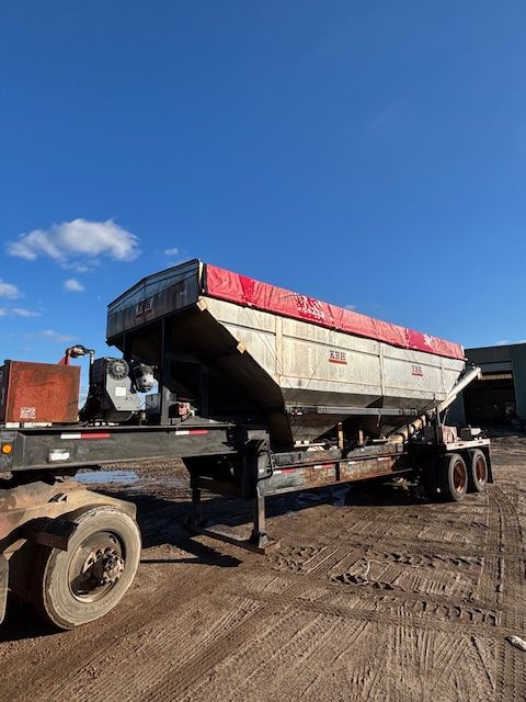 Large silver dump trailer with red tarp, parked outdoors on a dirt lot.