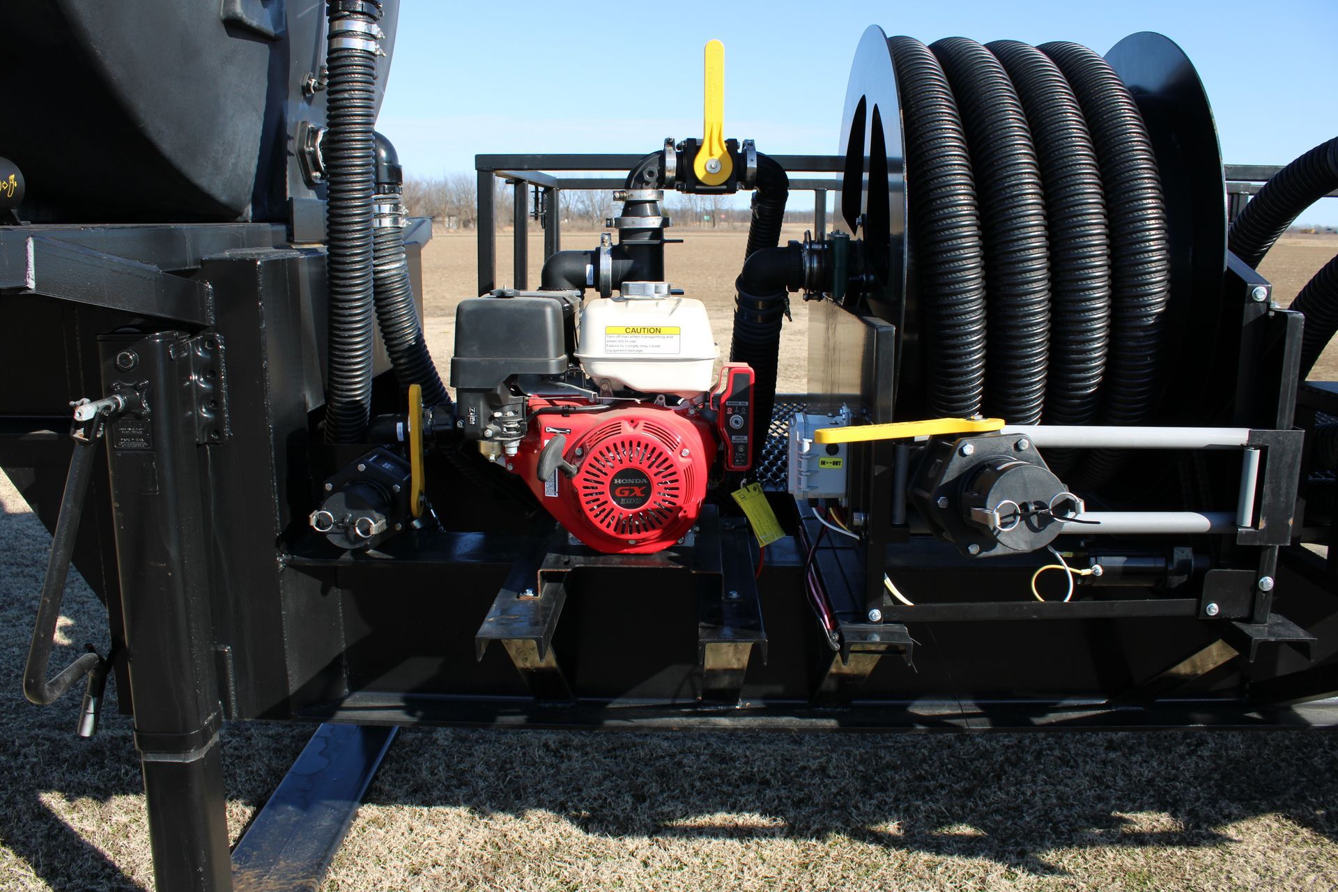 Black trailer with a red engine, hose reel, and yellow valves against a field.