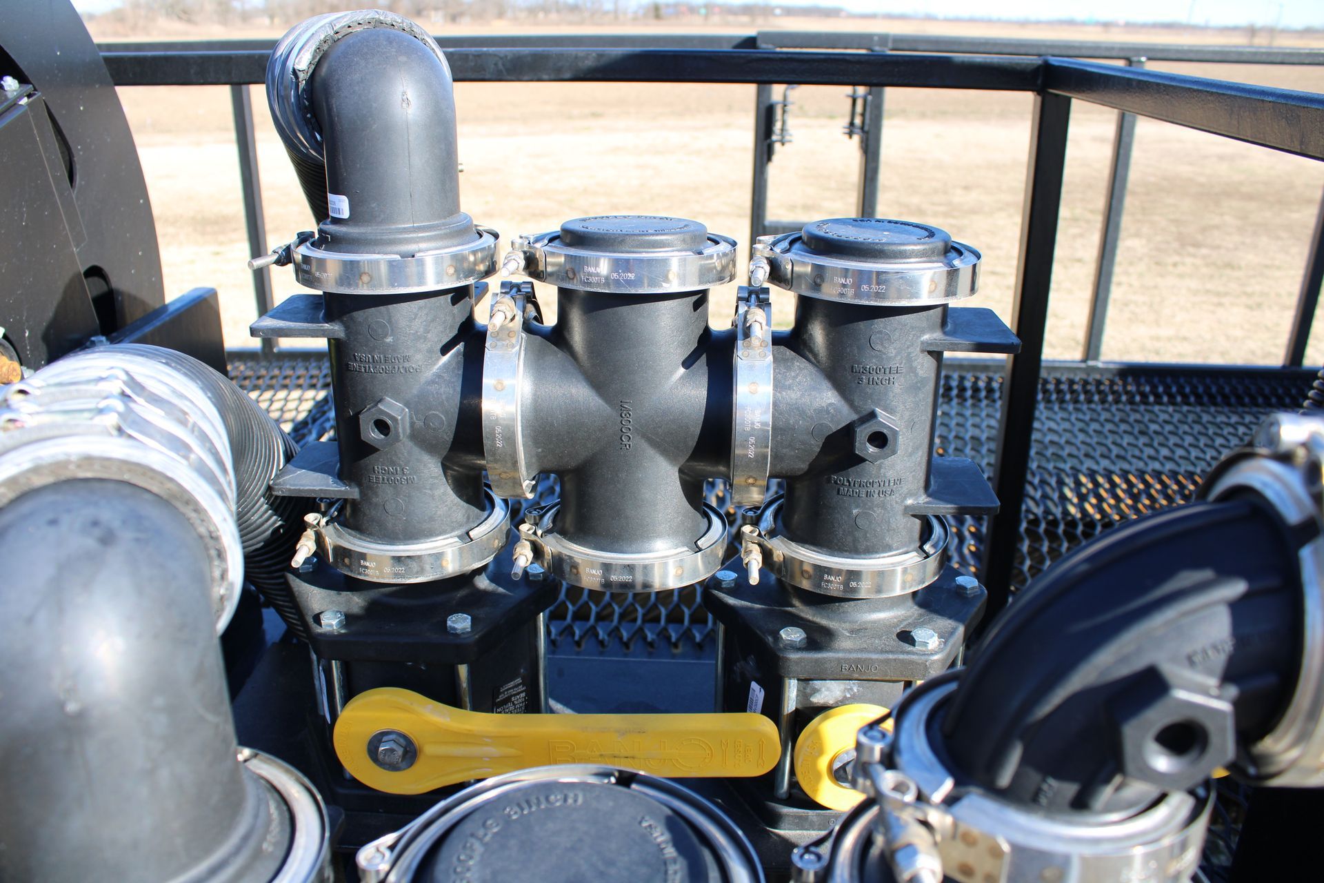 Close-up of three black pipes with silver connectors and yellow lever on a dark surface.
