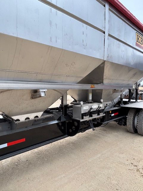 Silver grain trailer with black undercarriage and red top, parked on a paved surface.