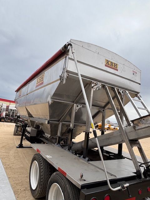 Silver KBH grain trailer with red tarp, parked outside on a cloudy day.