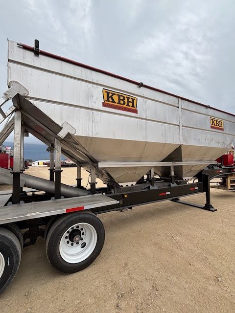 Silver KBH grain trailer with black frame, parked outdoors on a cloudy day.