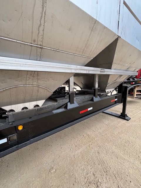Stainless steel grain trailer, black undercarriage, on concrete, side view.