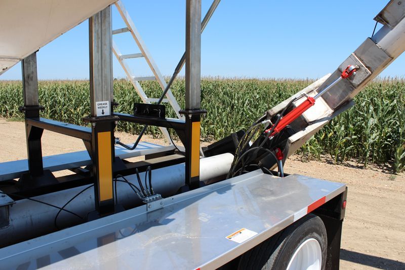 A trailer is parked in a field of corn.