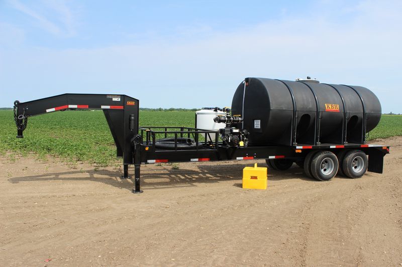 A trailer with a large tank attached to it is parked in a dirt field.