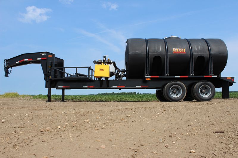 A trailer with a large tank on it is parked in a dirt field.