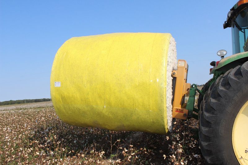 A tractor is carrying a large yellow bale of cotton