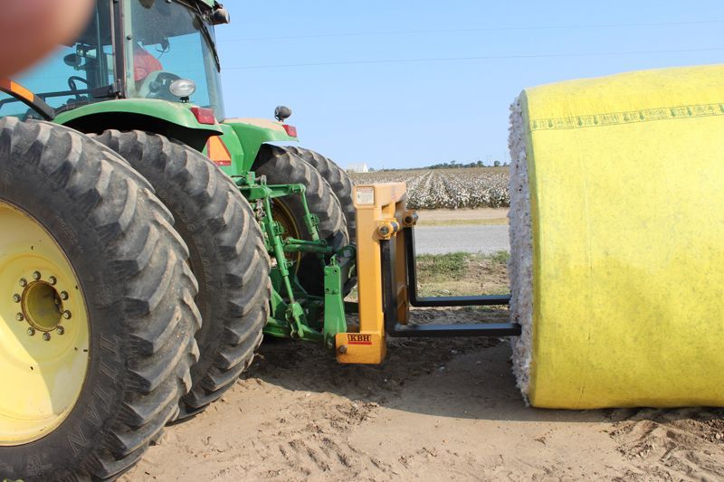 A john deere tractor is pulling a yellow bale of hay