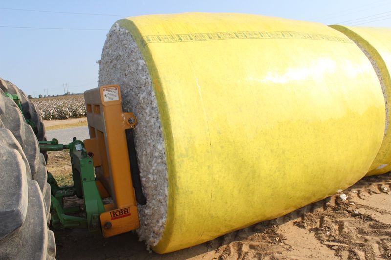 A yellow bale of hay is being rolled by a tractor.