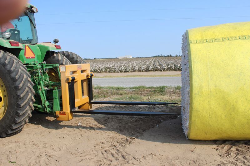 A green tractor is carrying a yellow bale of hay.