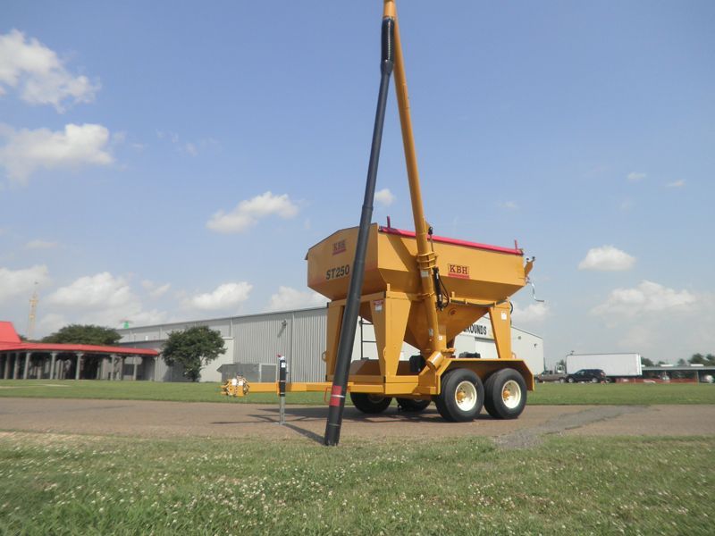 A large yellow trailer with a grain hopper on it is parked in a grassy field