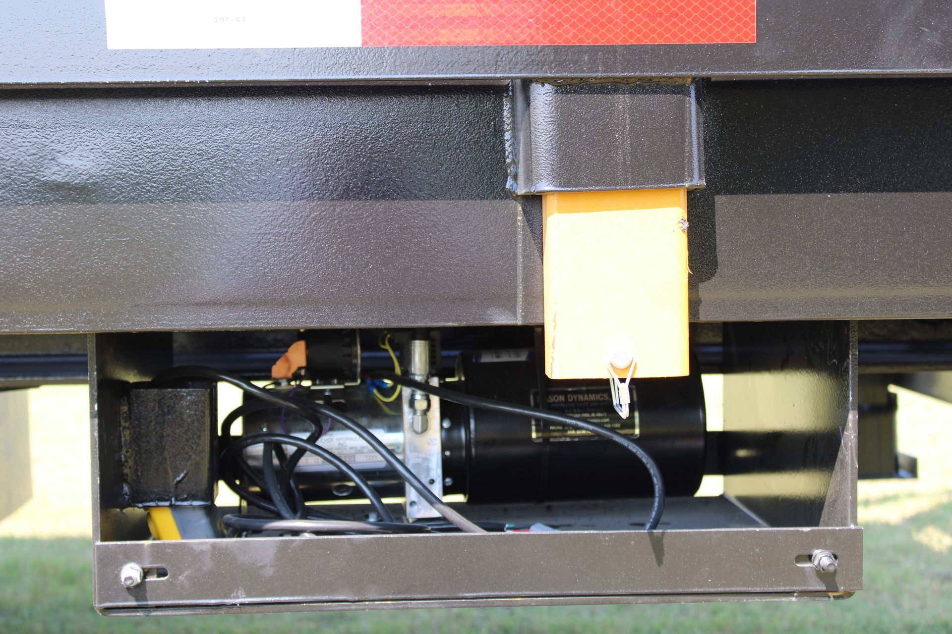 Close-up of a black trailer's undercarriage with a motor, wires, and a yellow tag.