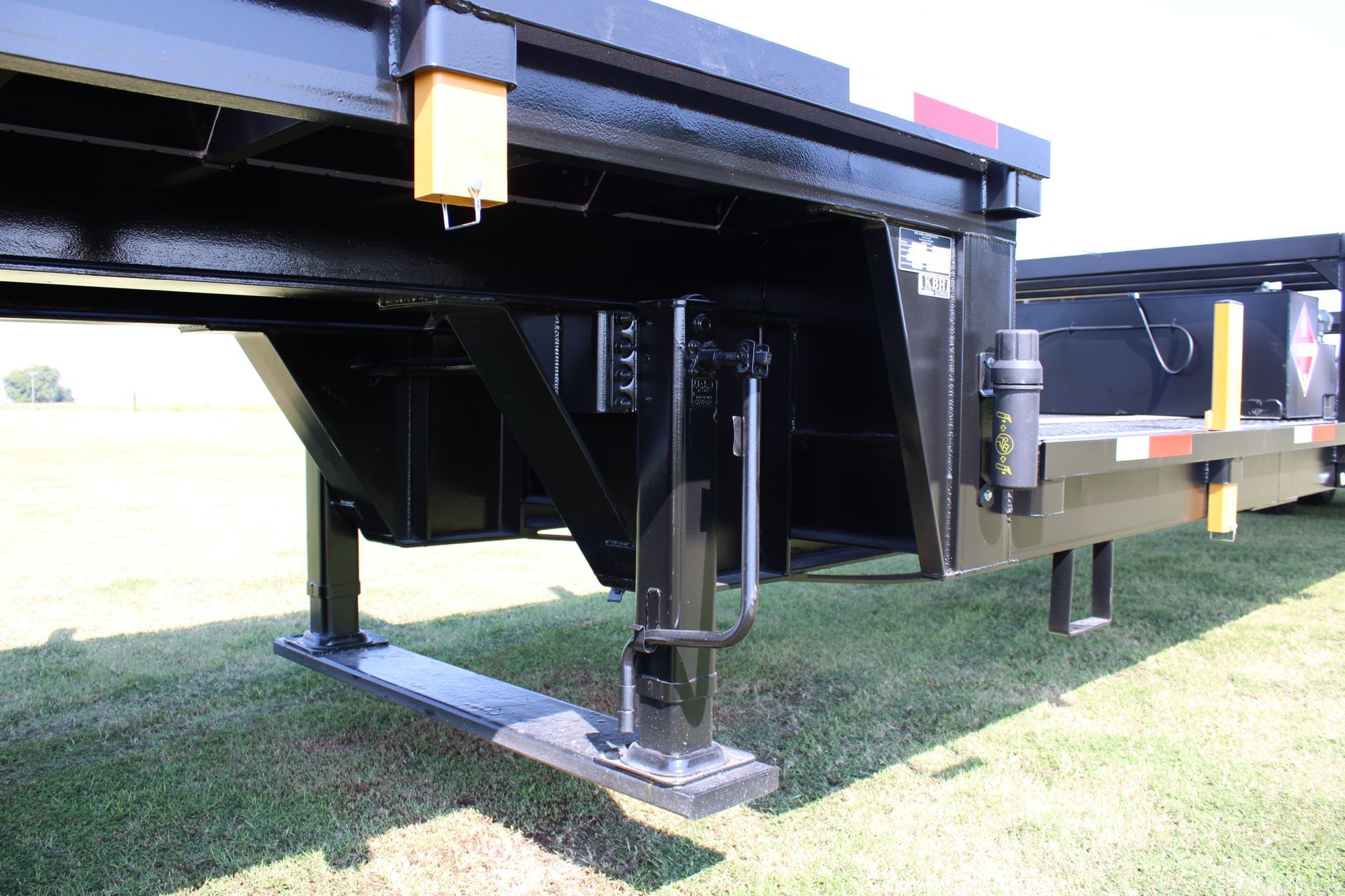 Black trailer with stabilizing legs lowered on a grassy field.