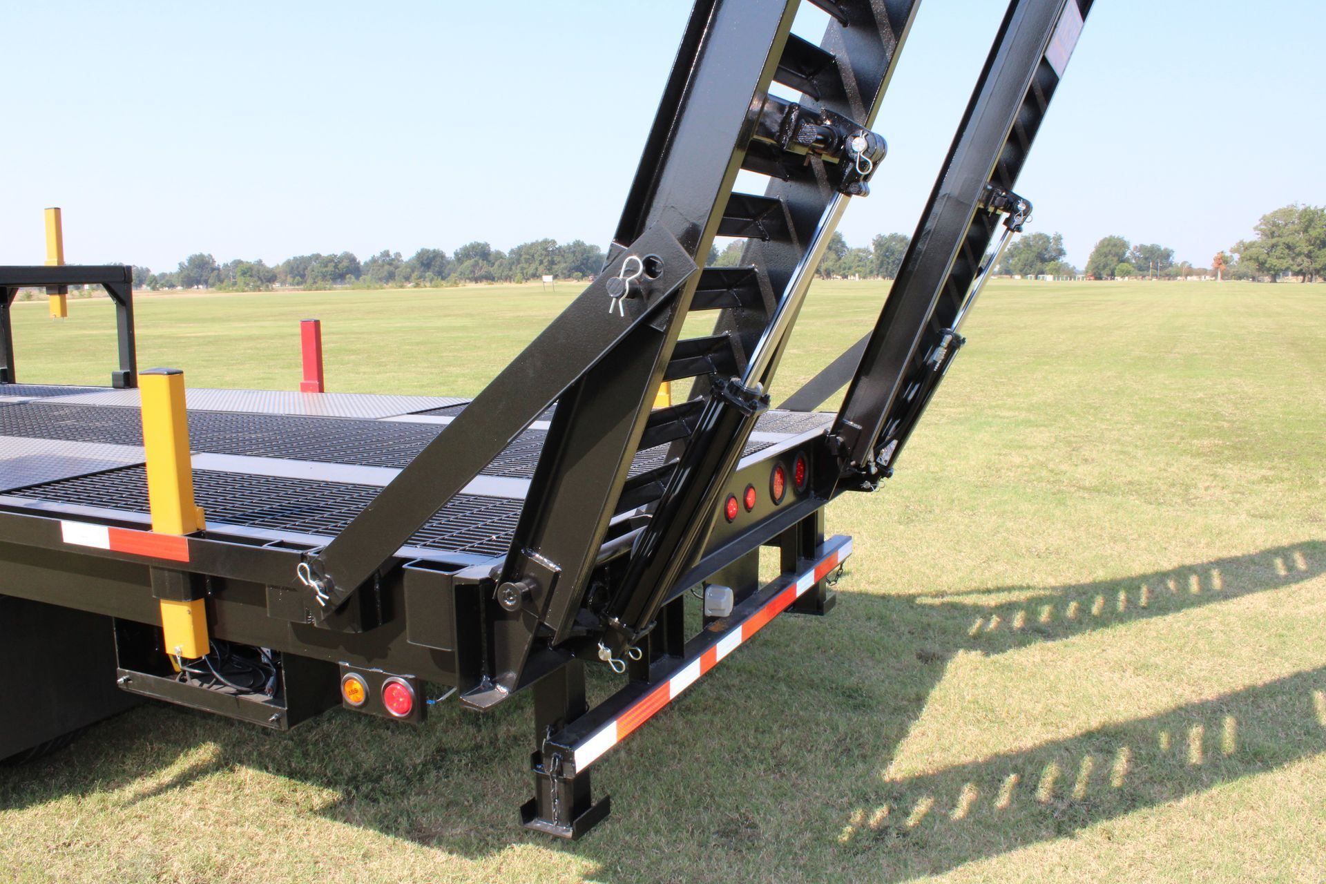 Black and yellow trailer with ramps lowered on a grassy field; sunny day.