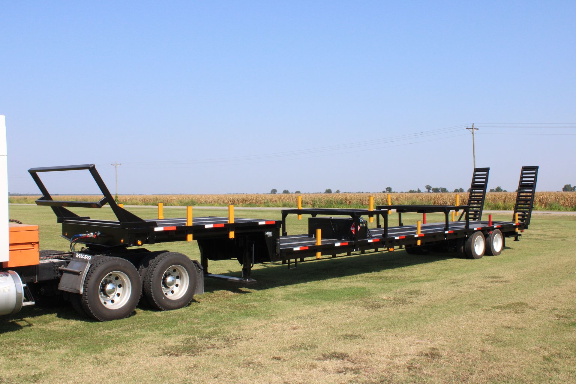 A semi truck with a trailer attached to it is parked in a grassy field.