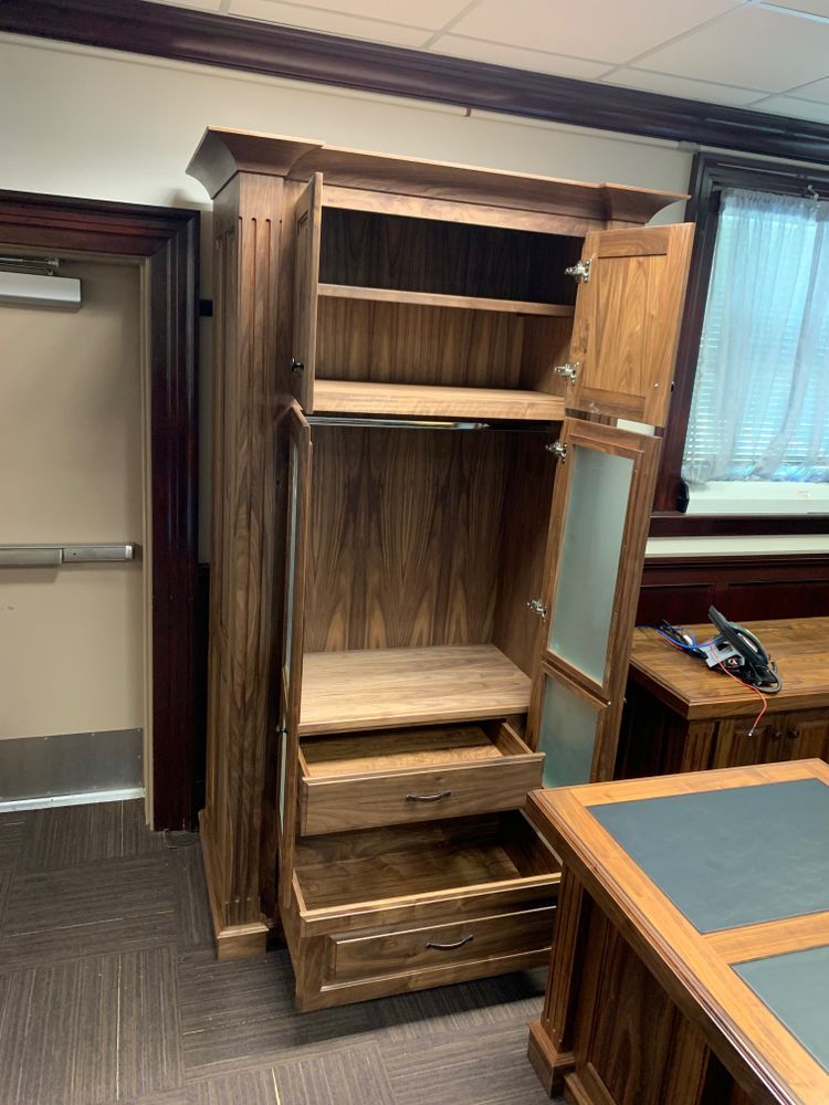 Wooden wardrobe with open doors, shelves, and drawers, in a room with a desk and door.