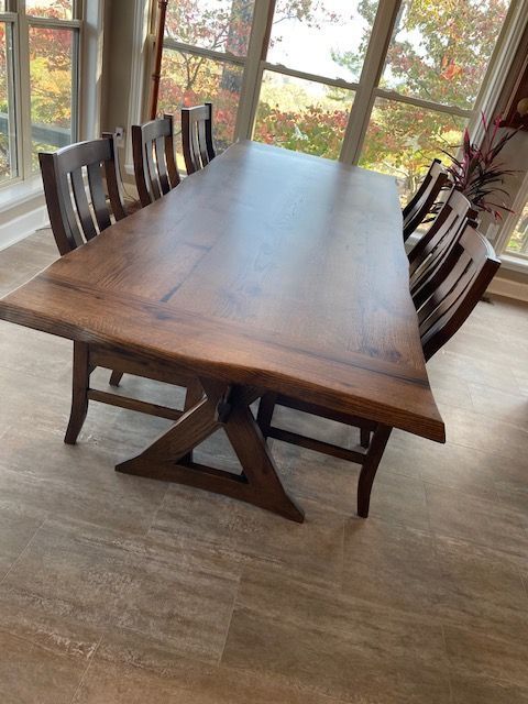 Wooden dining table with eight chairs, near a window overlooking trees.