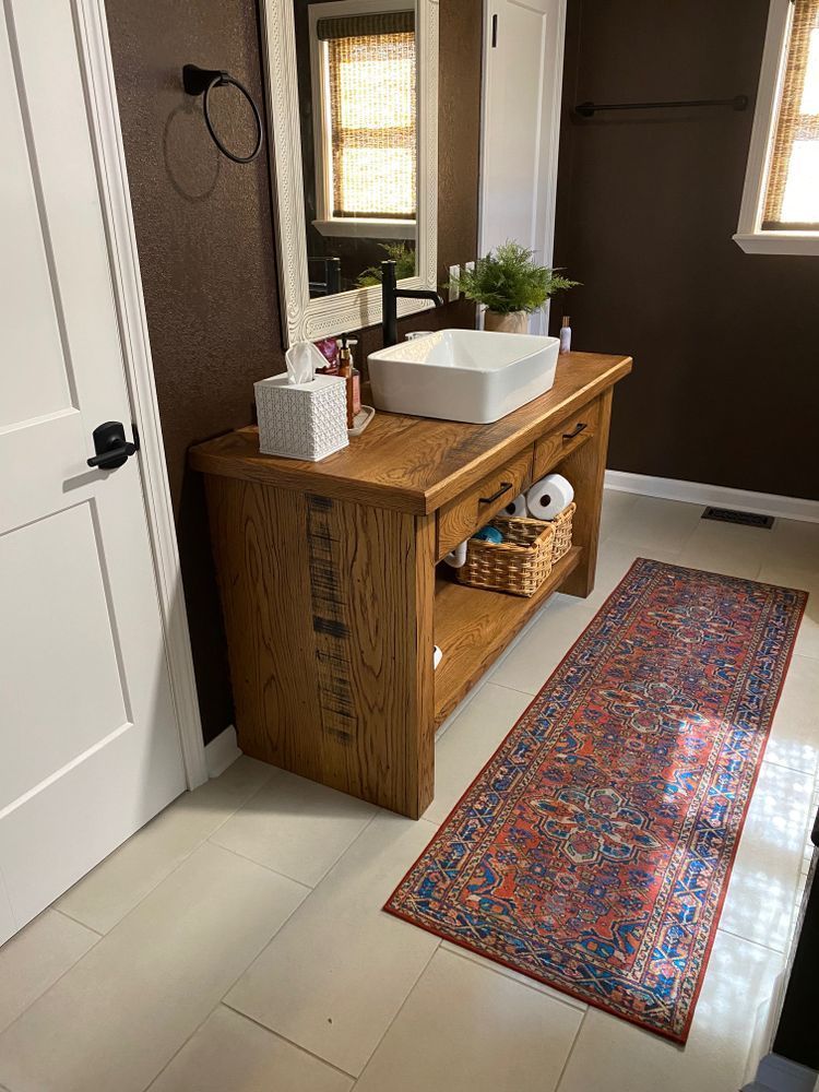 Bathroom with a wooden vanity, a white sink, and a colorful rug on the floor.