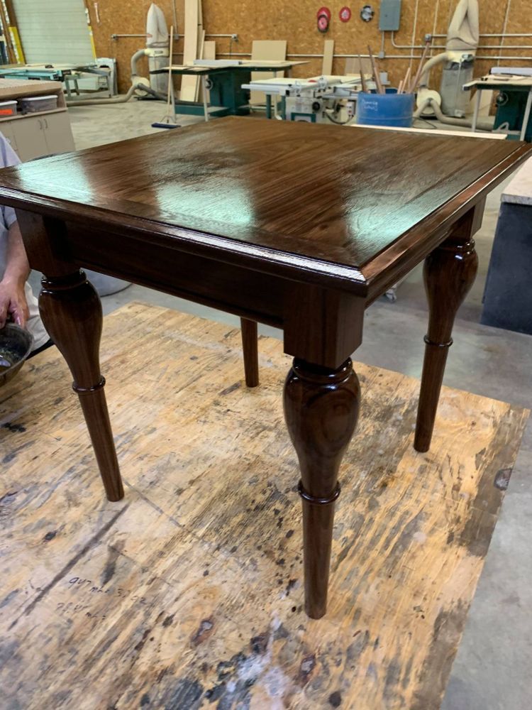 Dark wood square table with ornate legs, indoors in a workshop setting.
