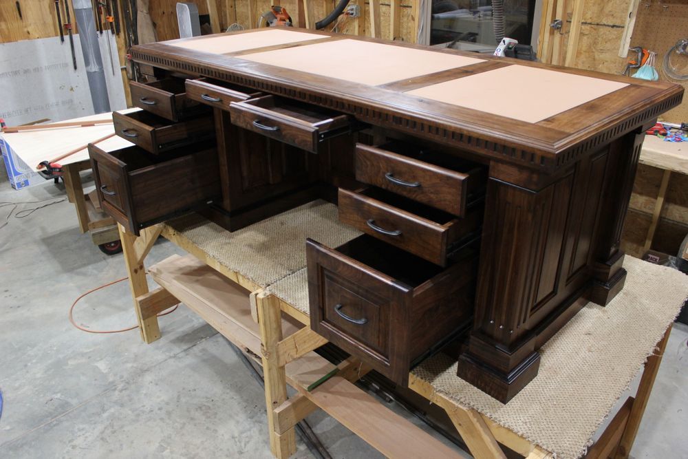 Dark wood desk with multiple drawers open on a workbench.