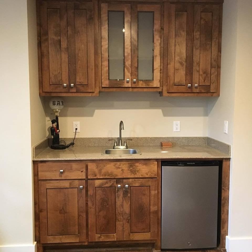 Built-in wooden bar with sink, upper cabinets, and a mini-fridge.