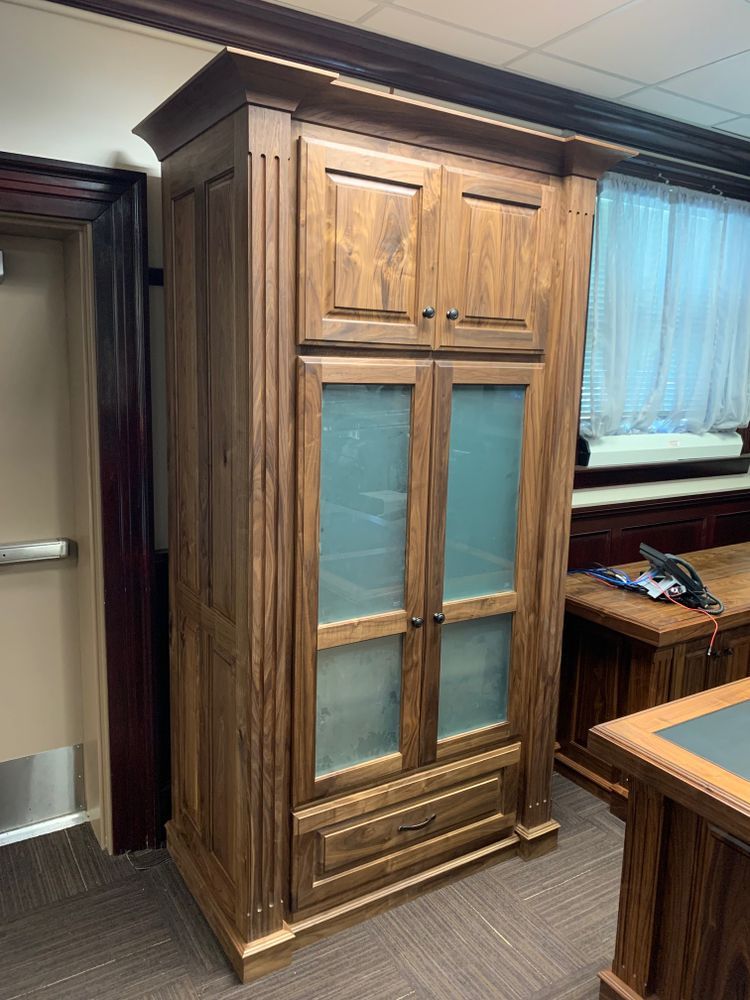 Tall wooden cabinet with glass doors, drawer, and paneled sides, in a room with a desk.