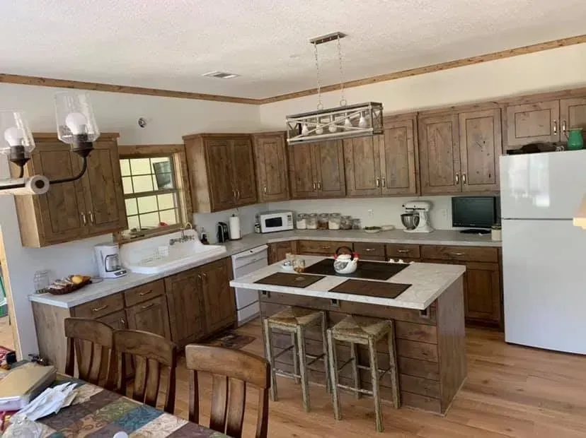 Kitchen with wooden cabinets, island with stools, white appliances, and a dining table.