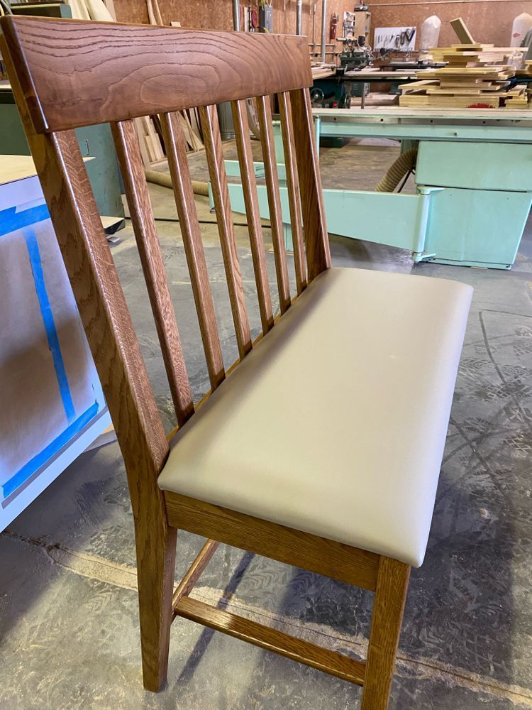 Wooden chair with light gray padded seat and vertical back slats, in a workshop setting.