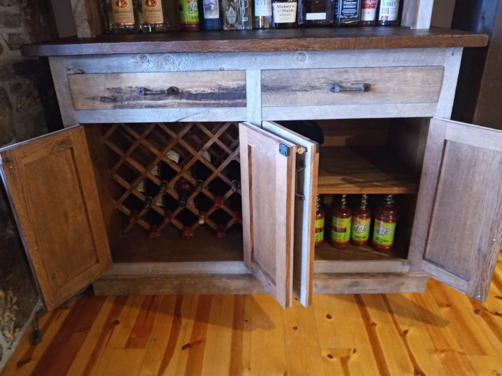 Wooden bar cabinet with wine rack, bottles, and open doors; wood floor.